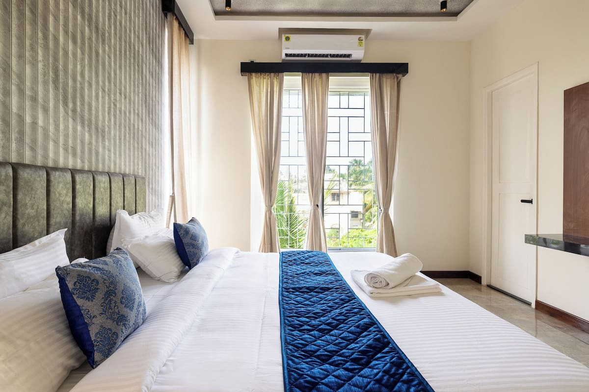 Ein Hotelzimmer mit einem großen Bett, einem Fenster mit Vorhängen, einer Klimaanlage und einer Tür.