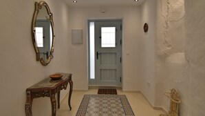 A hallway with a wooden console table, a decorative mirror, a patterned rug, and a door with a window. - Casa Los Anafes - in the heart of the village (Cómpeta)