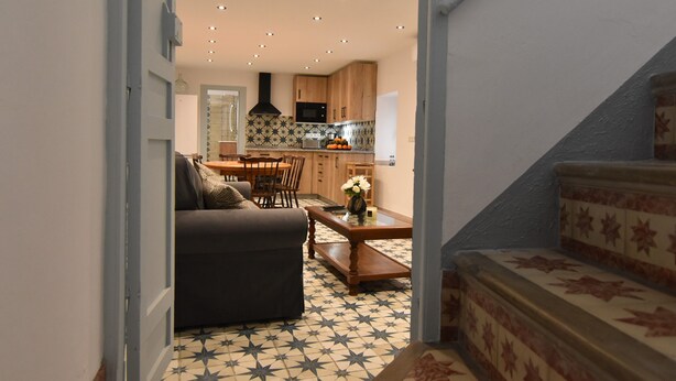 A modern kitchen with wooden cabinets, a dining area with a sofa, and a staircase with patterned steps. - Casa Los Anafes - in the heart of the village (Cómpeta)