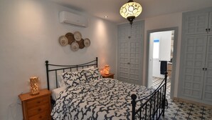 A bedroom with a bed, bedside tables, a wall-mounted air conditioner, and a door leading to another room. - Casa Los Anafes - in the heart of the village (Cómpeta)