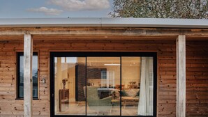 A modern building with a wooden facade, large sliding glass doors, and a visible interior with a fireplace and seating area. - Home Farm Holiday Homes (Nuneham Courtenay)