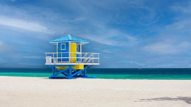 Una torre de salvavidas en una playa con agua turquesa cristalina y cielo azul.