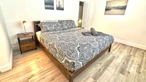 Un dormitorio con una cama de madera, una mesita de noche, una lámpara y dos cuadros colgados en la pared.