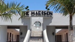 La entrada al hotel MADISON con una escalera que conduce a la entrada, palmeras y un cielo azul despejado.