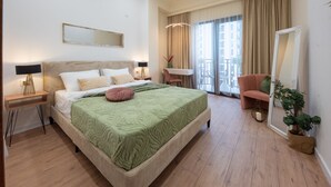 A hotel room with a large bed, a desk with a lamp, a chair, a balcony with a view, and a large mirror.