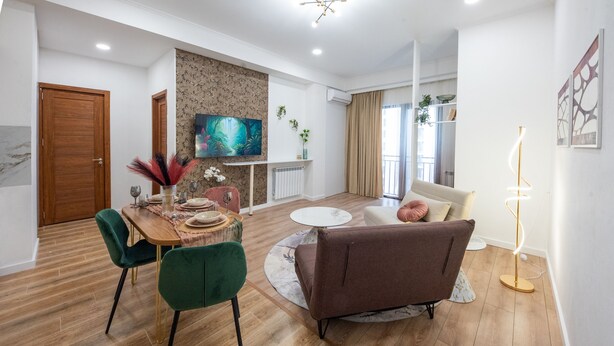 A modern living room with a dining area, wooden flooring, a sofa, a coffee table, and a TV.