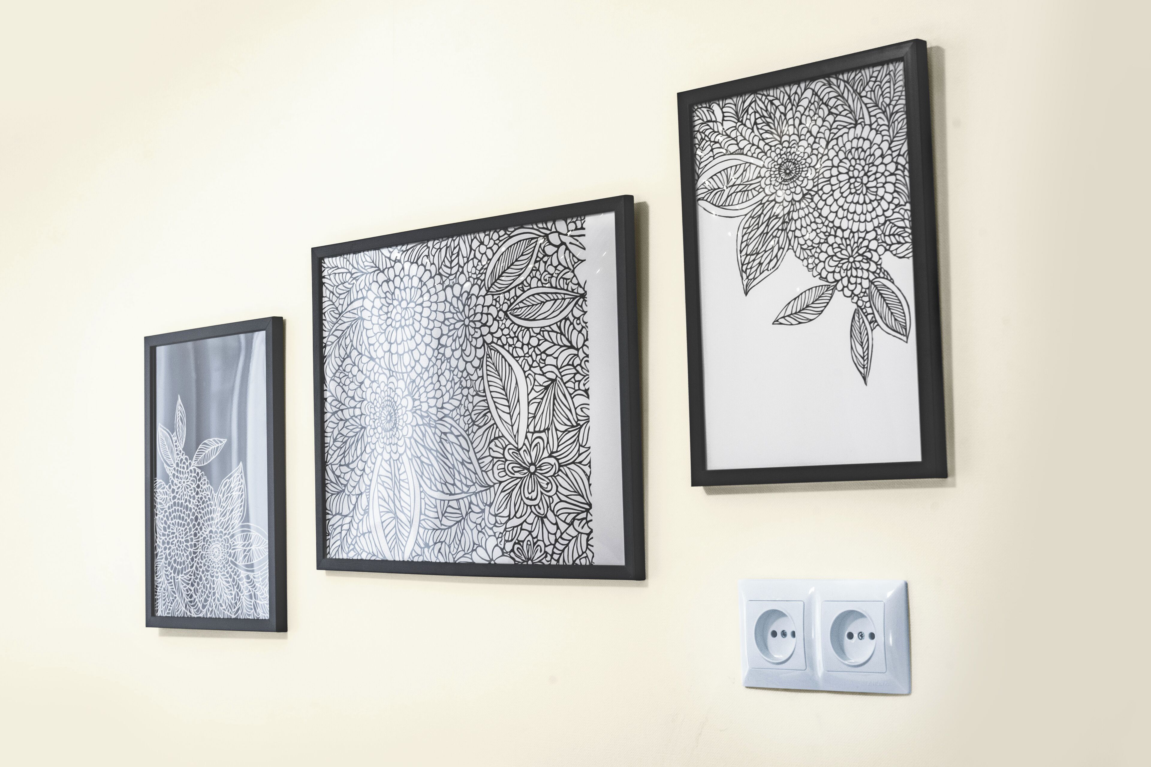 Três quadros em preto e branco com motivos florais em uma parede, com uma tomada elétrica abaixo.