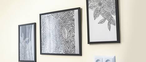 Três quadros em preto e branco com motivos florais em uma parede, com uma tomada elétrica abaixo.