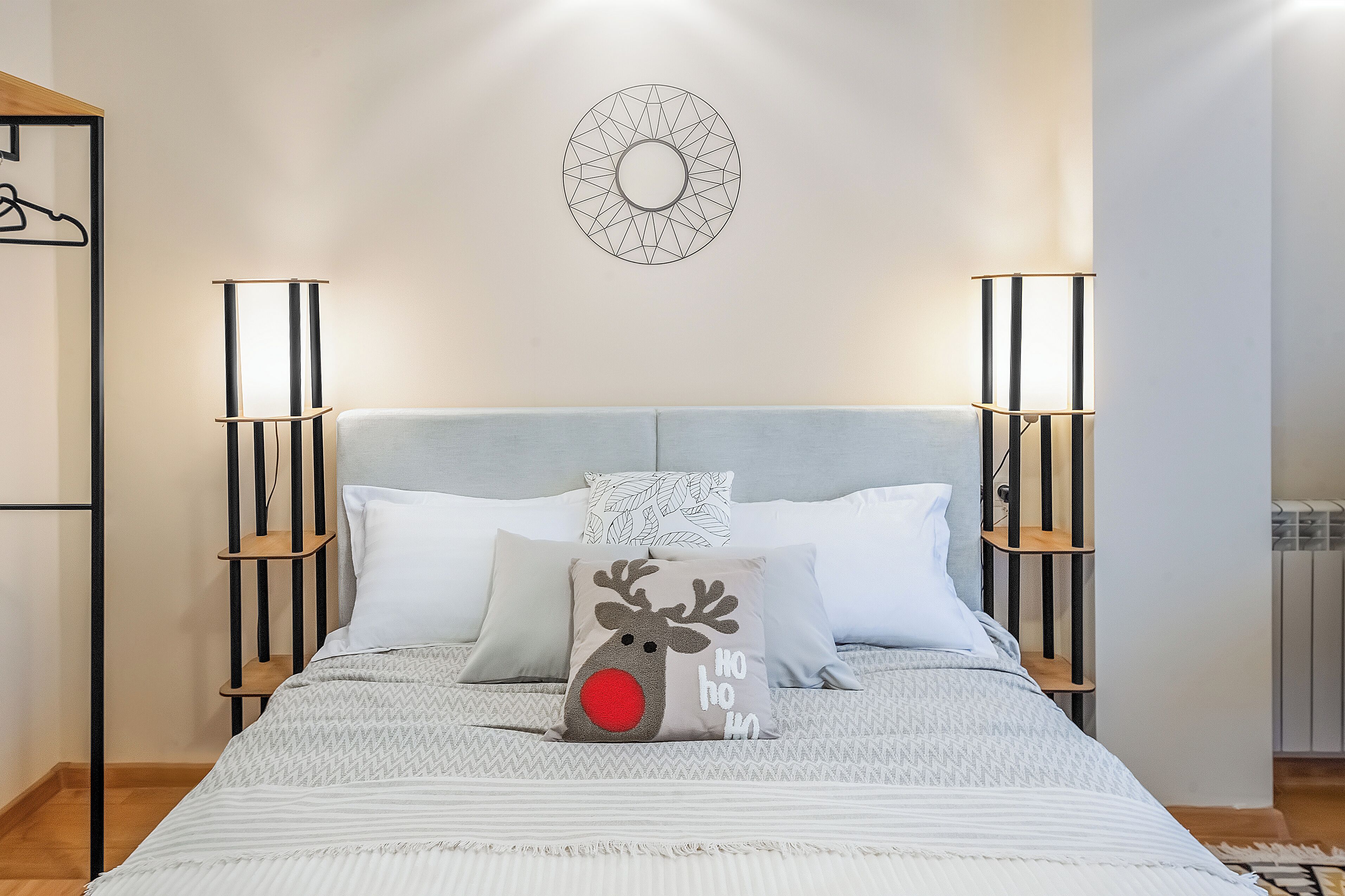 A neatly arranged bedroom with a bed, pillows, a wall clock, and bedside lamps.