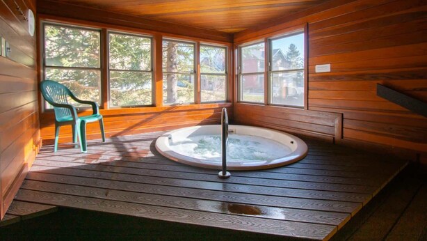 A wooden cabin with a hot tub, a chair, and large windows.