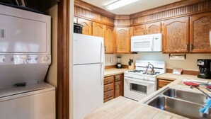 A compact kitchen with wooden cabinets, a white refrigerator, a microwave, a stove, and a sink.