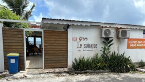 Un bâtiment avec une porte en bois, une enseigne indiquant « Gîtes Le Sunrise » et un appareil de climatisation.