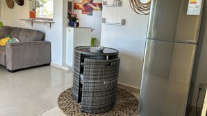 Une cuisine moderne avec un réfrigérateur en acier inoxydable, un canapé gris et un tonneau en osier.