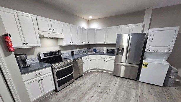 A modern kitchen with white cabinets, stainless steel appliances, and a grey wooden floor. - Private Apartment in Southbury 103 (Southbury)