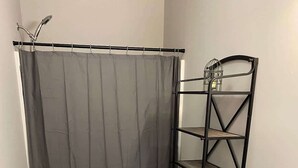 A bathroom with a shower curtain, a toilet, a metal shelf unit, and a white sink. - Private Apartment in Southbury 103 (Southbury)