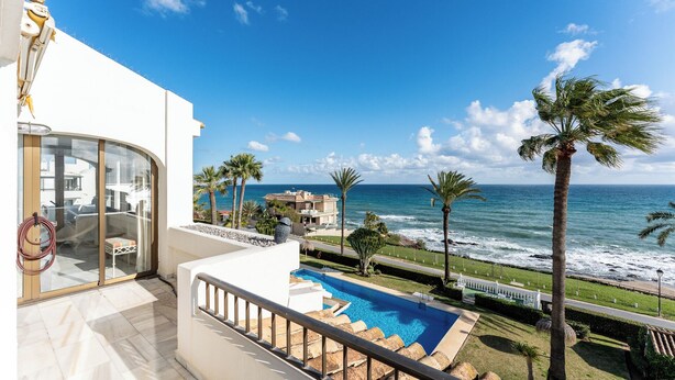 Ein Balkon mit Blick auf den Ozean, ein Schwimmbecken und Palmen.