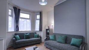 A living room with two grey sofas, each with green cushions, a coffee table, and a lamp on a side table.