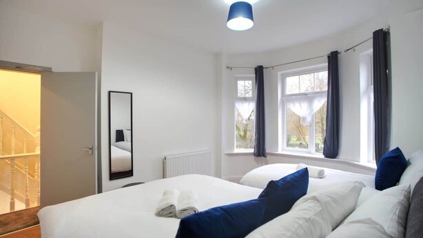 A hotel room with two beds, a large window with curtains, a mirror, and a ceiling light.
