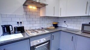 A compact kitchen with white cabinets, a gas stove, a microwave, and a coffee maker.