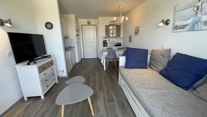 En moderne stue med et fladskærms-tv, en sofa med blå puder, et spisebord og et køkken i baggrunden.