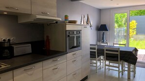 Une cuisine moderne avec des armoires blanches, un four encastré et un coin repas comprenant une table et des chaises.