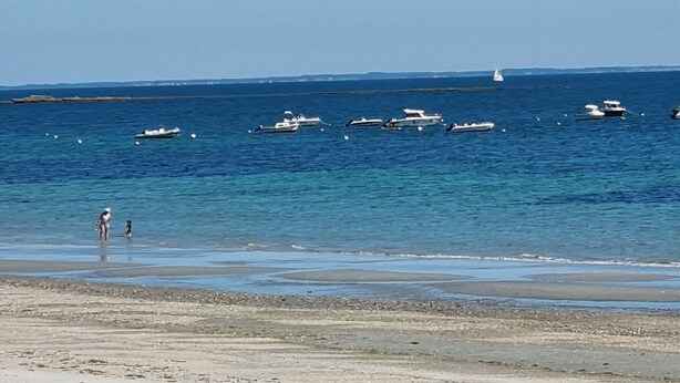 Une plage avec des bateaux sur l’eau et une personne qui se promène sur le rivage.
