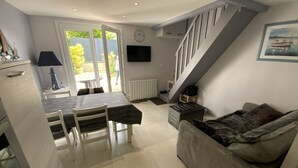 Un espace de vie compact comprenant un coin repas, un canapé, un escalier et un téléviseur fixé au mur.