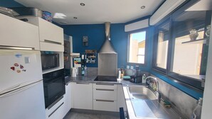 A modern kitchen with white cabinets, a built-in oven, microwave, and a large window providing natural light. - Renovated house with garden and terrace in La Chaume, near beach, WiFi (Les Sables-d'Olonne)