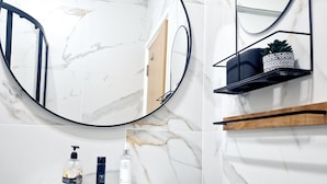 Un baño con lavamanos de mármol blanco, un espejo redondo y un mueble de madera debajo.