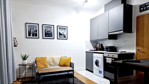 Un espacio habitable compacto con sofá, una mesita auxiliar, lavadora y kitchenette.