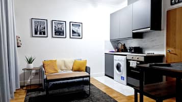 Cozy living area with a comfortable sofa and a potted plant, complemented by a sleek kitchen with modern appliances.