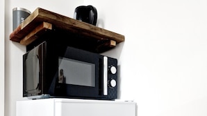 Un refrigerador blanco con microondas integrado en la parte superior, un estante de madera encima y un recipiente de acero inoxidable a la izquierda.