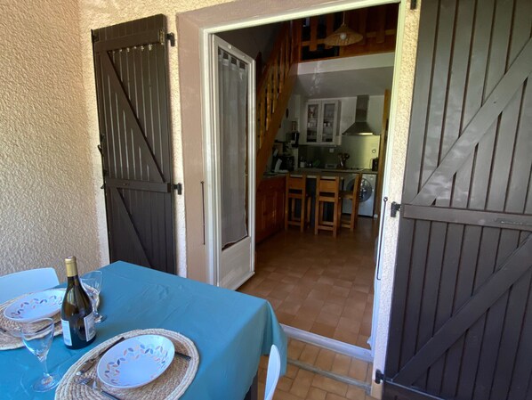 A dining area with a table set for two, a bottle of wine, and a view into a kitchen and dining area through open doors.