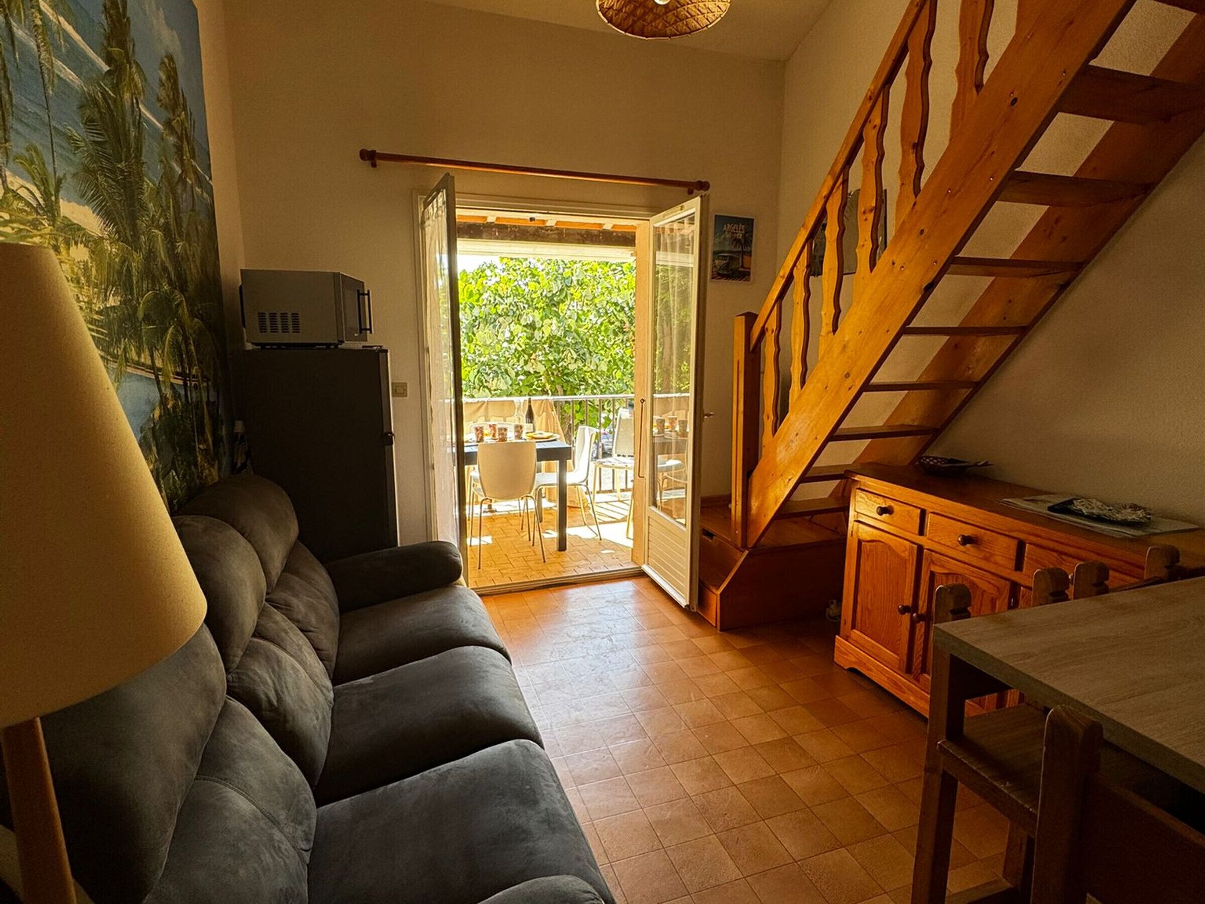 En hyggelig stue med sofa, spisebord, trappe og en skydedør til en udendørs terrasse.