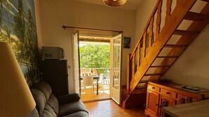 Una sala de estar acogedora con un sofá, una mesa de comedor, una escalera y un ventanal corredero que da a un patio exterior.