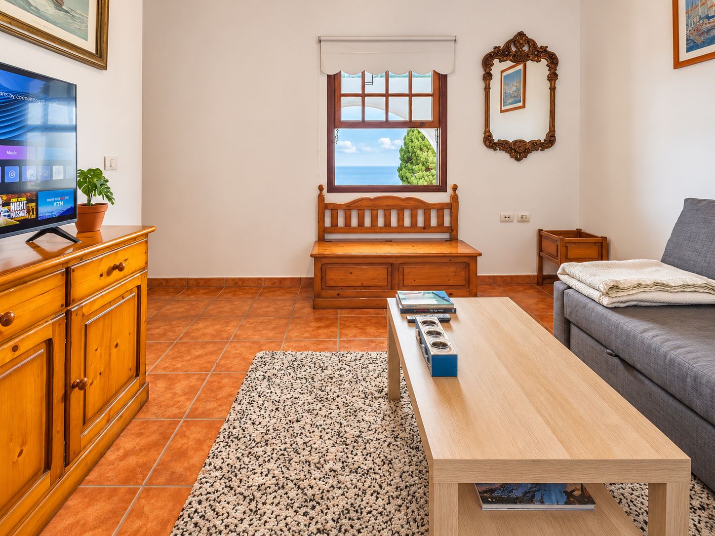Una sala de estar con un banco de madera, un sofá, una mesa de centro y un televisor sobre un mueble de madera.