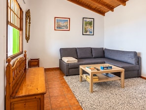 Una sala de estar acogedora con un banco de madera, un sofá gris, una mesa de centro con libros y un control remoto, y dos obras de arte enmarcadas en la pared.
