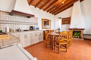 A kitchen with a wooden ceiling, tiled backsplash, and a dining area with wooden chairs and a table.