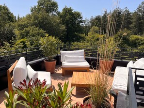 A rooftop terrace with a wooden bench, a white sofa, and potted plants.