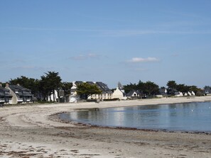 Ett kustområde med hus längs stranden, en sandstrand och stilla vatten.