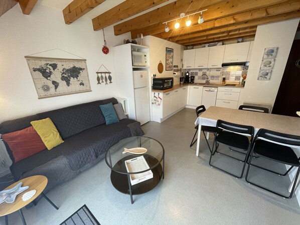 A compact living space with a kitchenette, a sofa, a dining table with chairs, and a small coffee table.