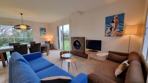 A modern living room with a blue sofa, a brown sofa, a dining area with a table and chairs, a TV, and a painting on the wall. - Modern house 6 people, near Crouesty Port and beaches, Wi-Fi, garden, ideal for families (Arzon)