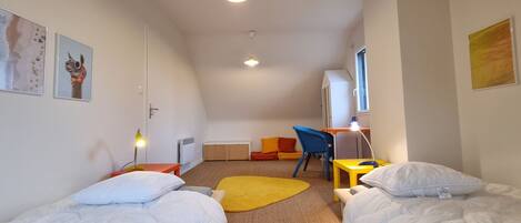 Een kamer met twee bedden, een bureau, een stoel, een radiator en een raam.