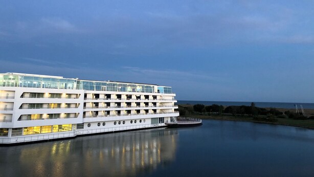 A large, multi-story cruise ship docked at a port with a modern white exterior and multiple decks.