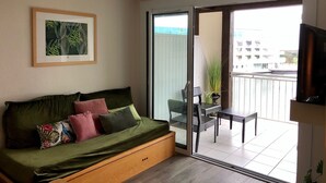 A modern living room with a green sofa, a framed botanical print, and a balcony with a table and chairs.