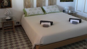 A neatly made bed with pillows and a blanket, a bedside table with a lamp, a wall clock, and a patterned floor. - Nicolashouse on the sea 2 (Bari)