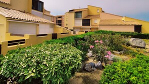 A residential building with multiple balconies, a garden with various plants, and a clear sky.