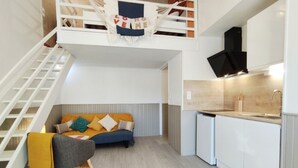 A compact living space with a loft bedroom, a sofa, a chair, and a kitchenette.