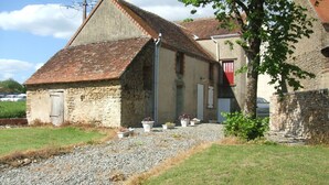 A stone building with a sloped roof, a gravel path leading to the entrance, and potted plants along the path.