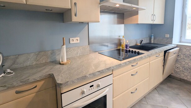 A modern kitchen with a built-in stove, oven, and sink. There are cabinets with silver handles and a window providing natural light.